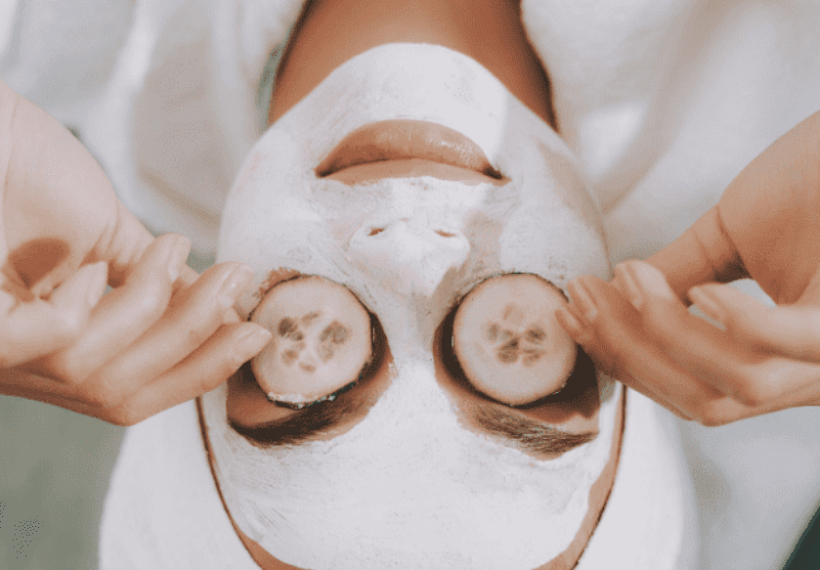 Une femme qui fait un masque visage avec des tranches de concombre sur les yeux pour enlever ses cernes